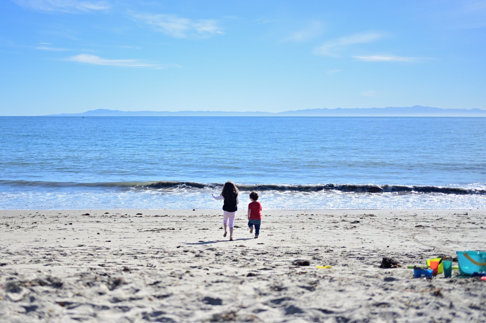 Two young children run toward the waves on a sunny Santa Barbara beach