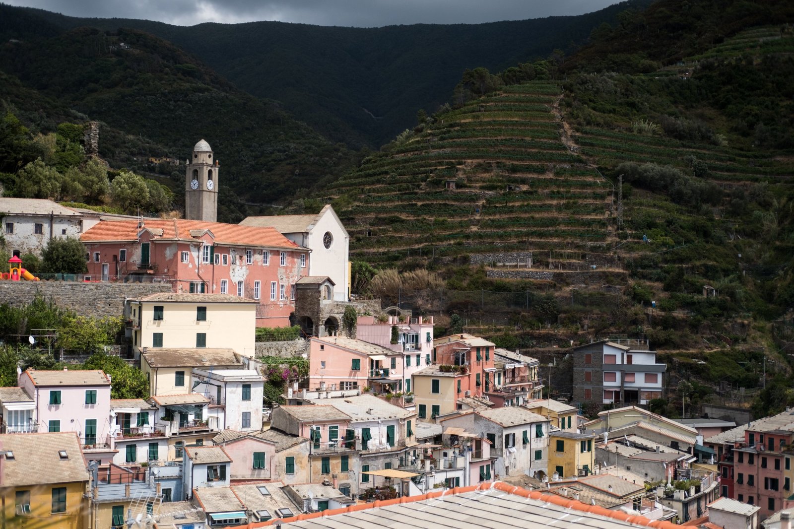 Pastel houses and a stone church tower below terraced hillsides in an Italian coastal village
